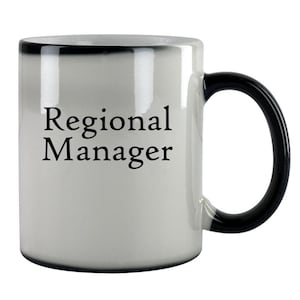 May include: White ceramic coffee mug with a black handle and rim. The mug has the text "Regional Manager" printed in black on the front.