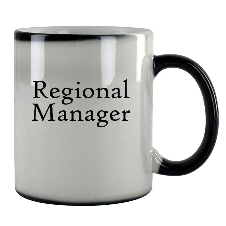 May include: White ceramic coffee mug with a black handle and rim. The mug has the text "Regional Manager" printed in black on the front.