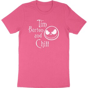 Op de afbeelding: Een roze t-shirt met de witte tekst "Tim Burton and Chill" en een witte afbeelding van een gezicht. Het shirt heeft korte mouwen en een ronde hals.