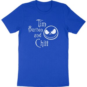 Op de afbeelding: Koningsblauw T-shirt met de witte tekst "Tim Burton and Chill" en een witte afbeelding van een gezicht. Het shirt is gemaakt van een zacht materiaal en heeft korte mouwen.