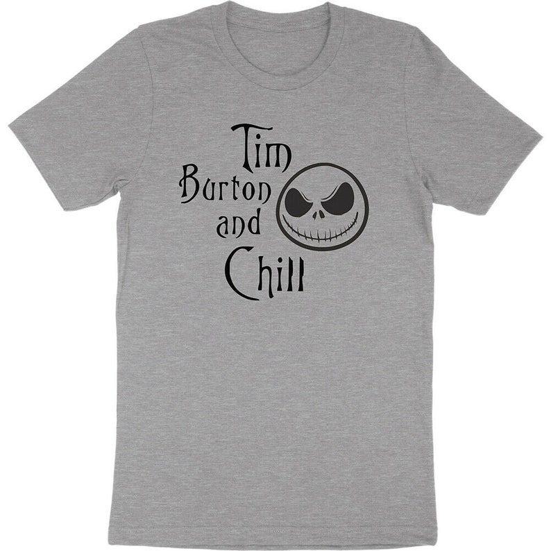 Op de afbeelding: Grijs T-shirt met de zwarte tekst "Tim Burton and Chill" en een Jack Skellington-gezicht. Het T-shirt heeft een ronde hals en is waarschijnlijk gemaakt van een zachte stof. Het ontwerp is een verwijzing naar regisseur Tim Burton.