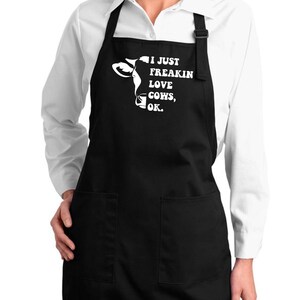 May include: Black apron with two front pockets and adjustable neck strap. The apron features a white graphic of a cow's head and the text "I JUST FREAKIN LOVE COWS, OK."