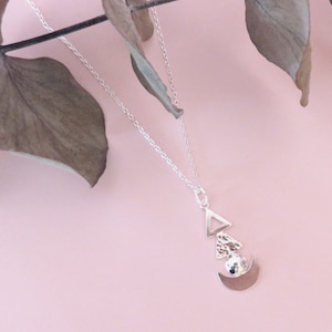 Può includere: Una collana d'argento con un ciondolo geometrico che presenta una mezzaluna, un triangolo e un cerchio testurizzato.