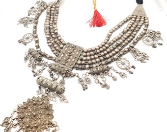May include: A silver necklace with multiple strands of beads and intricate pendants. The necklace features a large, ornate pendant with a starburst design and several smaller pendants with floral and geometric motifs.