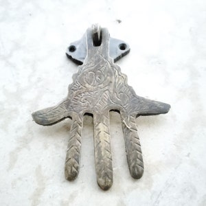 Könnte beinhalten: Ein Türklopfer aus Messing in Form einer Hand mit aufwendigen, geätzten Designs. Der Türklopfer hat einen Ring, der oben befestigt ist, und ist auf einer schwarzen Metallplatte montiert.