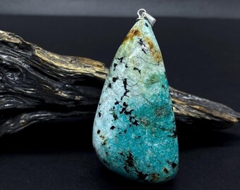 May include: A turquoise pendant with a silver bail, featuring a unique pattern of blue, green, and brown hues. The gemstone is displayed against a dark background with a piece of driftwood. The pendant is a natural stone.