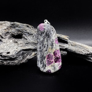 以下が含まれることがあります： ピンクと白のインクルージョンが入った濃いグレーの石で作られたペンダント。石は涙の形をしていて、シルバーのベイルが付いています。