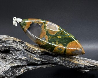 May include: A green, brown, and white patterned stone pendant with a silver bail. The pendant is resting on a piece of driftwood.