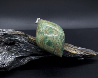 May include: A green and brown stone pendant with a silver bail. The pendant is shaped like a teardrop and has a marbled pattern. The pendant is sitting on a piece of driftwood.