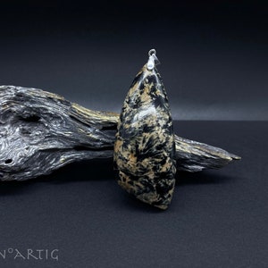 May include: A black and gold stone pendant with a silver bail. The stone has a swirling pattern and is shaped like a teardrop.