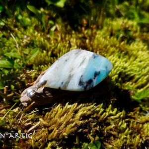 Può includere: Un ciondolo blu chiaro e bianco con macchie nere, incastonato in argento, su un letto di muschio.