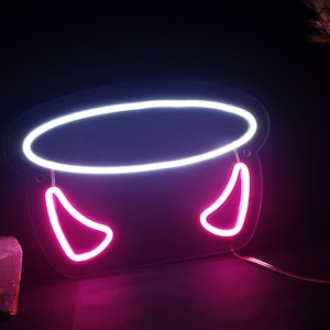 Puede incluir: Un letrero de neón con forma de caldero con luces de neón blancas y rosas. El caldero tiene dos cuernos rosas a los lados.