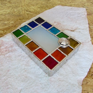 Peut inclure: Une sonnette en argent avec un motif en vitrail. Le verre est dans des tons de vert, bleu, jaune, orange, rouge et marron. Le bouton de la sonnette est rond et argenté.