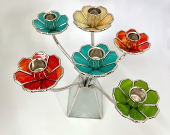 Könnte beinhalten: Ein silberner Kandelaber mit sechs bunten Glasblumen-Kerzenhaltern. Die Blumen sind türkis, gelb, orange, rot, grün und blau.