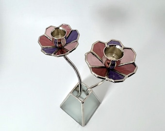 Könnte beinhalten: Ein silberner Kerzenhalter mit zwei rosa und violetten, blumenförmigen Kerzenbechern. Der Kerzenhalter hat eine weiße Basis.