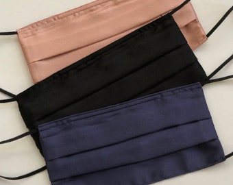 Op de afbeelding: Drie gezichtsmaskers van satijn. De maskers zijn in verschillende kleuren: roze, zwart en blauw.