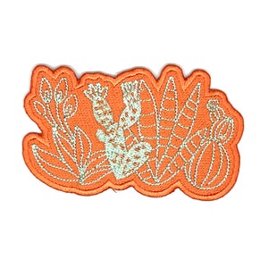 May include: An orange embroidered patch with a white outline of various plants, including a cactus, leaves, and flowers.