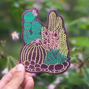 Può includere: Toppa ricamata con un giardino di cactus colorato con cactus verdi, rosa e gialli su uno sfondo viola.