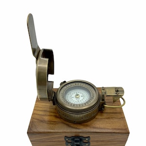 Peut inclure: Une boussole vintage en laiton avec un couvercle à charnière, présentée sur une boîte en bois. Le cadran de la boussole comporte un cadran détaillé avec des indications directionnelles. La boîte a une finition en bois foncé et un fermoir en métal.