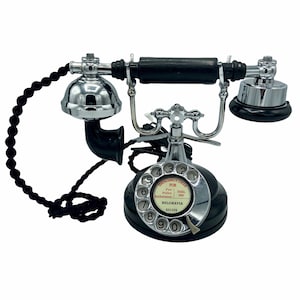 Pode incluir: Um telefone rotativo preto com acabamento cromado. O telefone tem um dial rotativo com os n&uacute;meros de 1 a 0 e um pequeno r&oacute;tulo branco que diz "EMERGENCY CALLS FOR Fire Police Ambulance DIAL 999 BELGRAVIA 8512256".