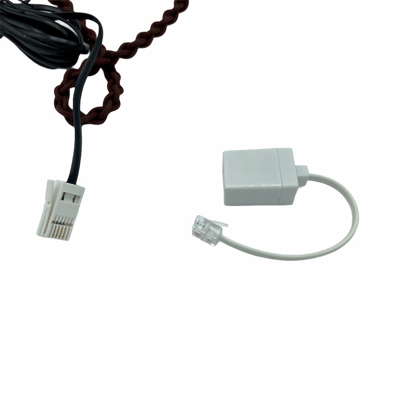 Pode incluir: Um adaptador de telefone branco com um conector RJ-11 branco e um conector RJ-11 cinza. O adaptador est&aacute; conectado a um cabo de telefone preto.