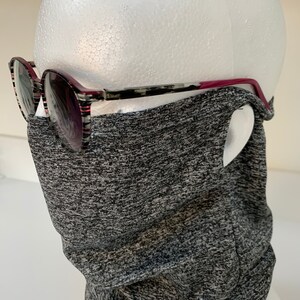 May include: A gray and black neck gaiter made of a stretchy fabric. The gaiter is worn on a mannequin head with a pair of black and red glasses.