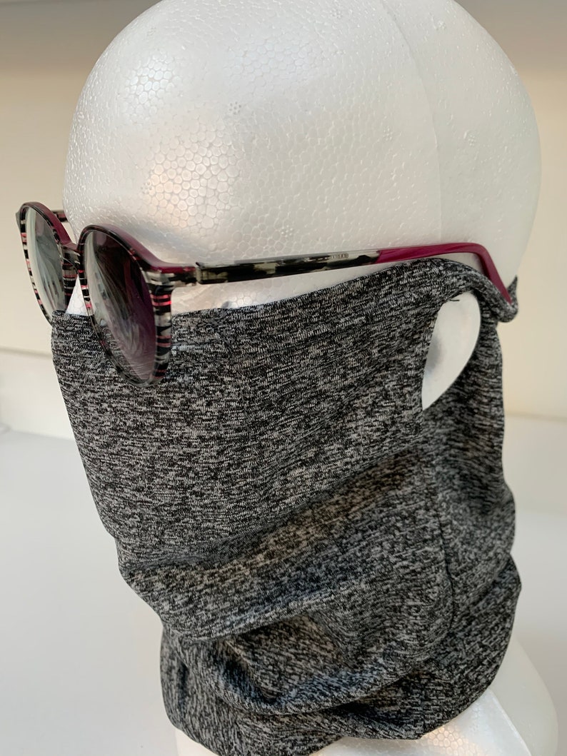 May include: A gray and black neck gaiter made of a stretchy fabric. The gaiter is worn on a mannequin head with a pair of black and red glasses.