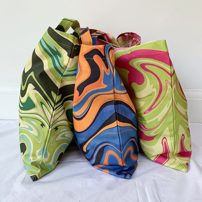 May include: Three tote bags with colorful, swirled patterns. One bag features green and black swirls, another has orange and blue, and the third displays pink and green. Each bag has a matching handle.