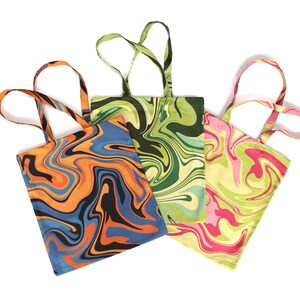 May include: Three tote bags with colorful, swirled patterns. One bag features orange, black, and blue swirls, another has green and cream swirls, and the third has pink and green swirls. Each bag has matching handles.