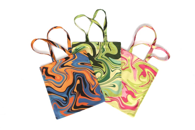 May include: Three tote bags with colorful, swirled patterns. One bag features orange, black, and blue swirls, another has green and cream swirls, and the third has pink and green swirls. Each bag has matching handles.