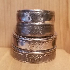 May include: Four silver rings stacked on top of each other. Each ring has the words "TEXAS 1845" engraved on the side.