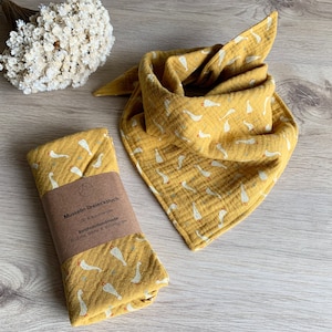 Könnte beinhalten: Zwei gelbe Musselin-Babyspucktücher mit einem weißen Gänseprint. Die Spucktücher sind aus 100% Baumwolle und handgefertigt. Der Text auf dem Etikett lautet "Musselin Dreiecktuch 100% Baumwolle  Ratzfatzhandmade find me @etsy & instagram".