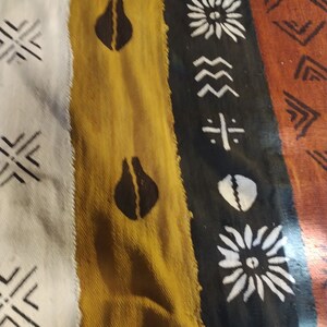 May include: A close-up of a woven fabric with a colorful striped pattern. The fabric features geometric shapes and designs in black, white, brown, yellow, and orange.