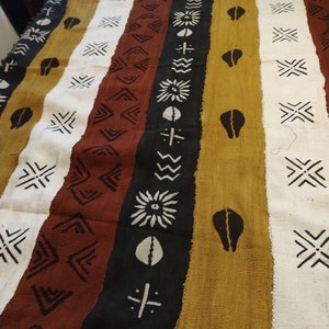 May include: A woven tapestry with a repeating geometric pattern in black, white, brown, and gold. The tapestry has a fringe border.