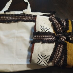 May include: A white tote bag with black trim and a brown and white patterned fabric with black trim. The fabric has a geometric design.