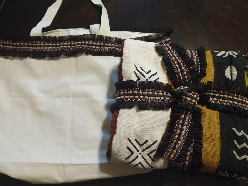May include: A white tote bag with black trim and a brown and white patterned fabric with black trim. The fabric has a geometric design.
