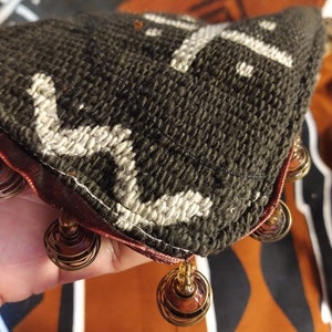 May include: A black and white patterned fabric pillow with a burgundy trim and brown beaded fringe.