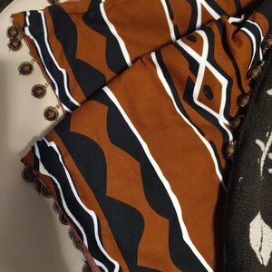 May include: A brown and black fabric with a geometric pattern. The fabric has a white trim and is decorated with gold beads.