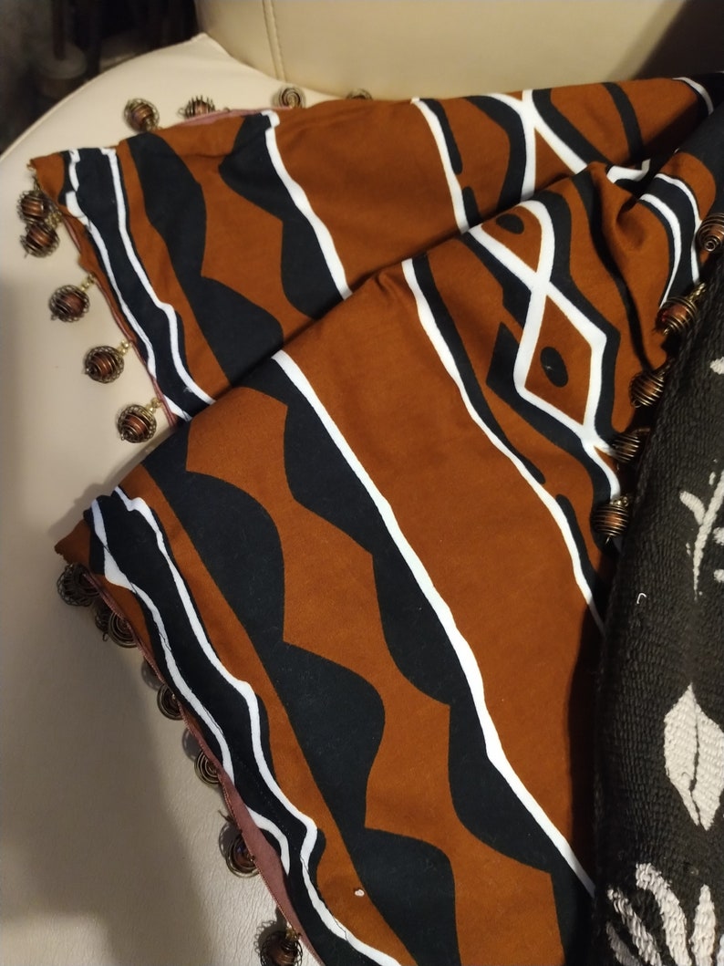 May include: A brown and black fabric with a geometric pattern. The fabric has a white trim and is decorated with gold beads.