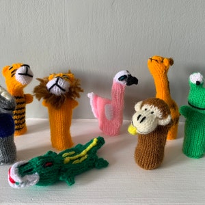 Puede incluir: Un conjunto de ocho marionetas de dedos de punto que representan varios animales, entre ellos un tigre, un león, un flamenco, una jirafa, un mono, una rana y un cocodrilo. Las marionetas están hechas con hilo de colores y tienen rasgos faciales detallados.