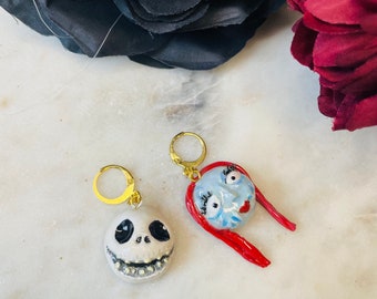 May include: A pair of handmade polymer clay earrings featuring the faces of Jack Skellington and Sally from the movie The Nightmare Before Christmas. The earrings are attached to gold hoop earrings.