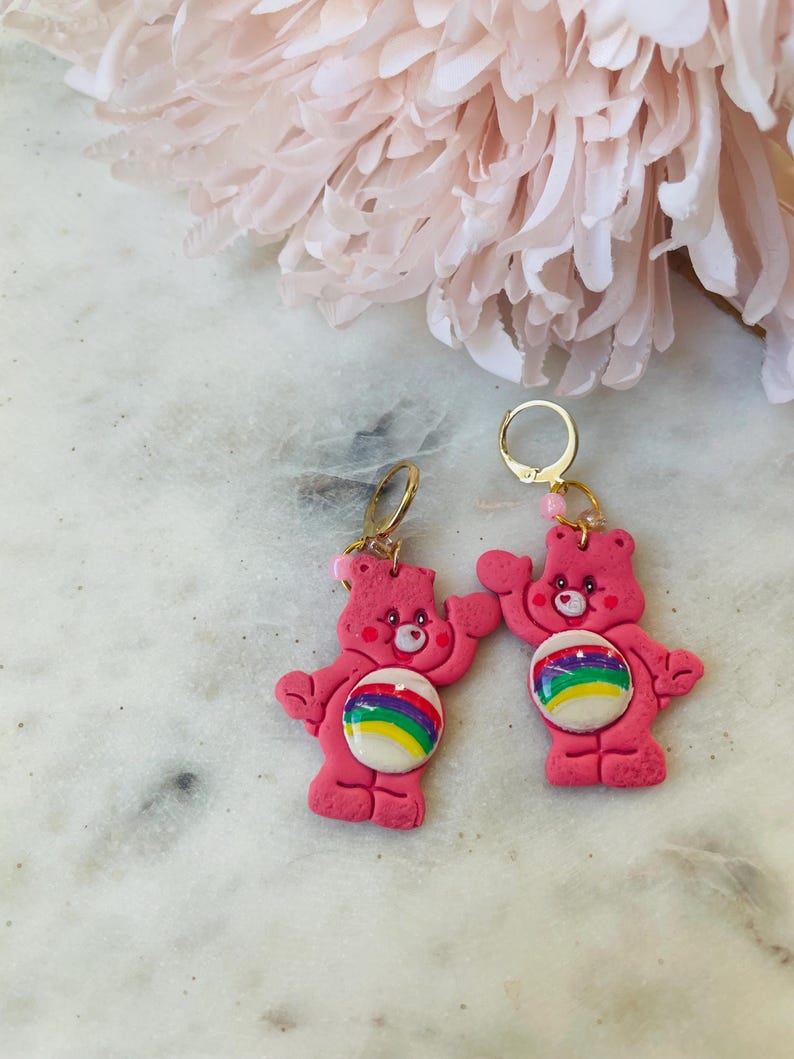 May include: Pink Care Bear earrings with rainbow belly buttons and gold hoops.