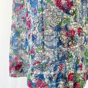 Close up of the hem A vintage 1940's floral print shirtwaist dress with short sleeves and a button-down front. The dress features a collared neckline and a midi-length skirt. The fabric is semi-sheer and has a blue, red, and green floral pattern that resembles stained glass. The dress is displayed on a mannequin against a white backdrop.