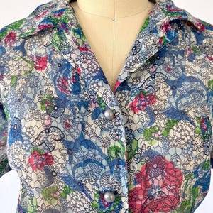Close up of the neckline A vintage 1940's floral print shirtwaist dress with short sleeves and a button-down front. The dress features a collared neckline and a midi-length skirt. The fabric is semi-sheer and has a blue, red, and green floral pattern that resembles stained glass. The dress is displayed on a mannequin against a white backdrop.