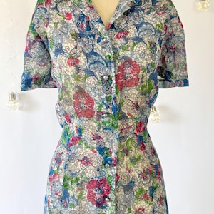 Close up of the bodice A vintage 1940's floral print shirtwaist dress with short sleeves and a button-down front. The dress features a collared neckline and a midi-length skirt. The fabric is semi-sheer and has a blue, red, and green floral pattern that resembles stained glass. The dress is displayed on a mannequin against a white backdrop.
