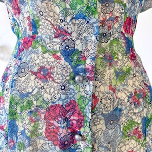 Close up of the waist A vintage 1940's floral print shirtwaist dress with short sleeves and a button-down front. The dress features a collared neckline and a midi-length skirt. The fabric is semi-sheer and has a blue, red, and green floral pattern that resembles stained glass. The dress is displayed on a mannequin against a white backdrop.