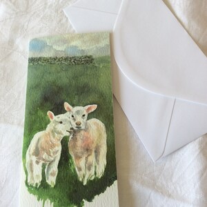 May include: A watercolor painting of two white lambs in a green field. The lambs are facing each other and appear to be nuzzling. The background is a green field with a stone wall in the distance.