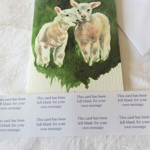 May include: A watercolor painting of two white lambs standing in a green field. The card has been left blank for a message.