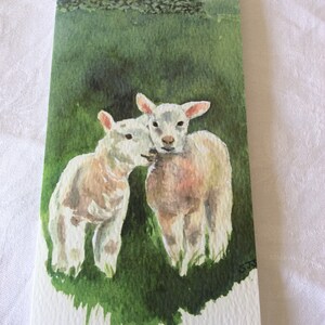 May include: Watercolor painting of two white lambs in a green field. The lambs are facing each other and appear to be nuzzling. The background is a green field with a stone wall and a cloudy sky.