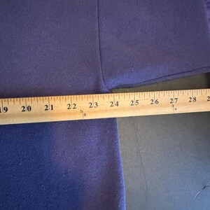 May include: A close-up of a dark blue fabric with a wooden ruler placed across it. The ruler measures from 19 to 28 inches. The fabric appears to be a piece of clothing, possibly a shirt or sweater.